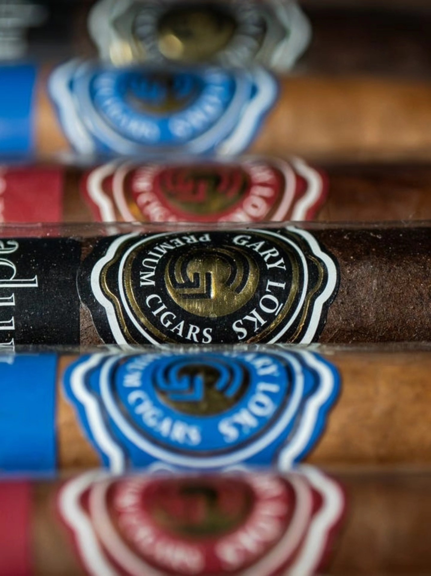 Gary Lōks Premium Cigars box and banded cigars displayed on a wooden surface with bourbon barrels in the background