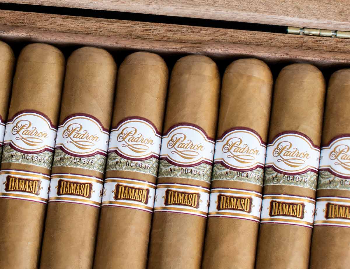 A Padrón Dámaso cigar with Ecuadorian Connecticut wrapper resting beside a cup of Cuban coffee on a wooden surface